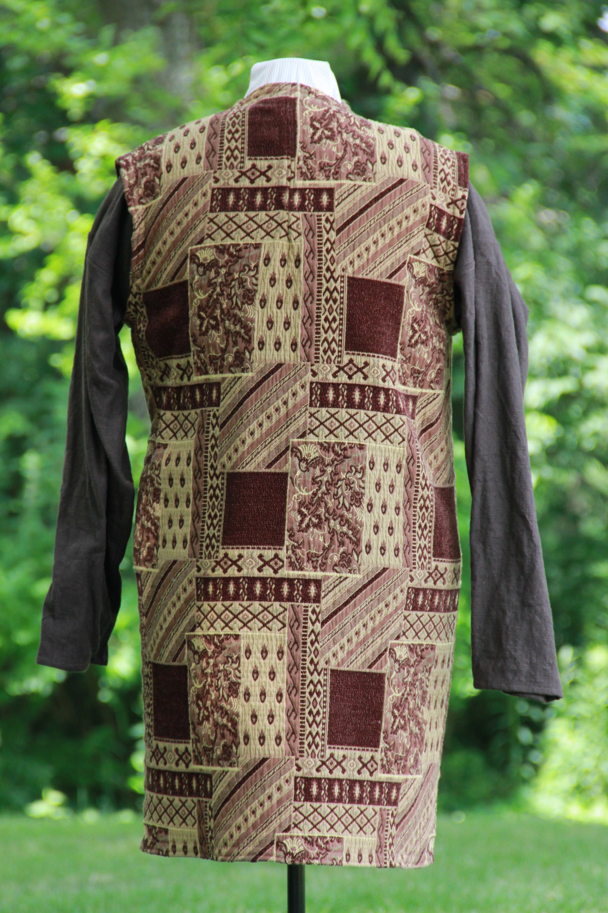 A hand made patchwork patterned chenille medieval jerkin in brown with leather and wooden hand carved toggles by west creek craftsman. Back view